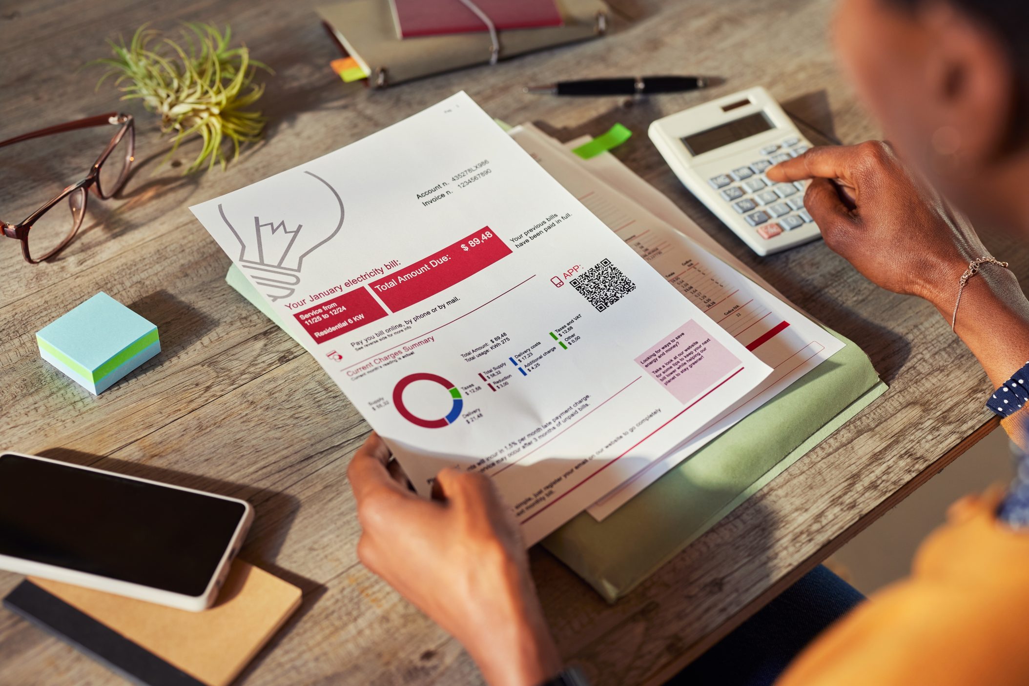 Top view of african american woman holding and calculating electricity bill at home. Rear view of african american woman T2G - calculating the increase of the bills in the last few months. Using calculator to check electricity cost at home.